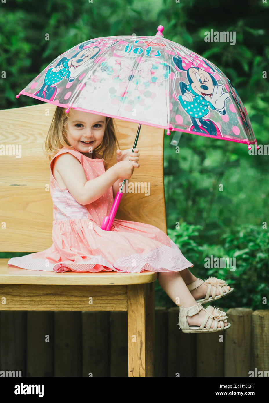 Jeune fille blonde assise sous un parasol dans le jardin coloré Banque D'Images