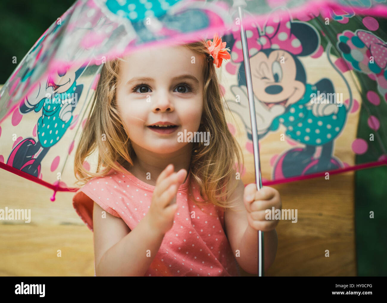 Jeune fille blonde assise sous un parasol dans le jardin coloré Banque D'Images