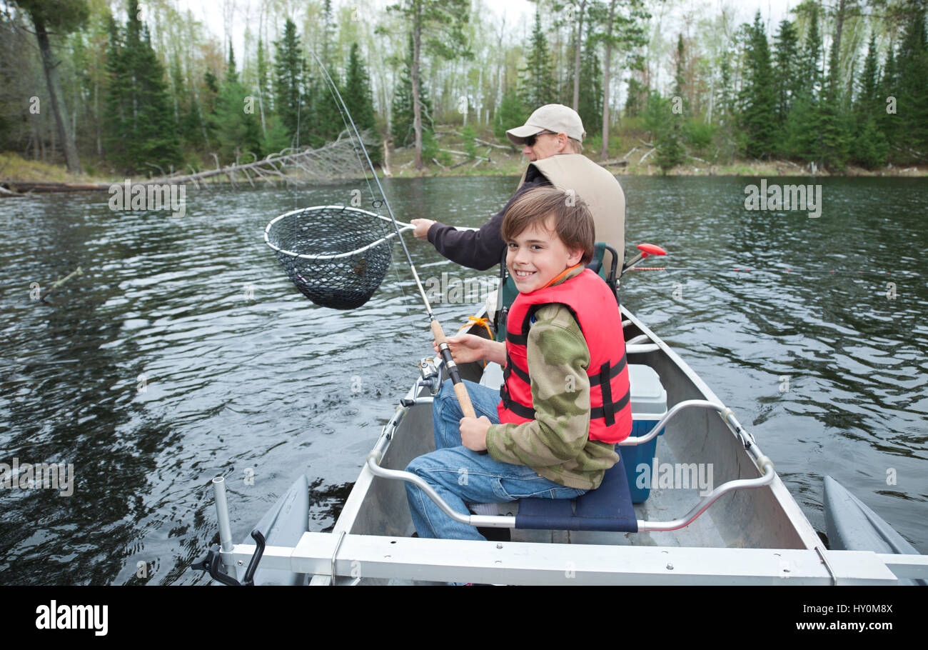 Un jeune pêcheur dans un canot sourit après avoir vu son filet de doré Banque D'Images