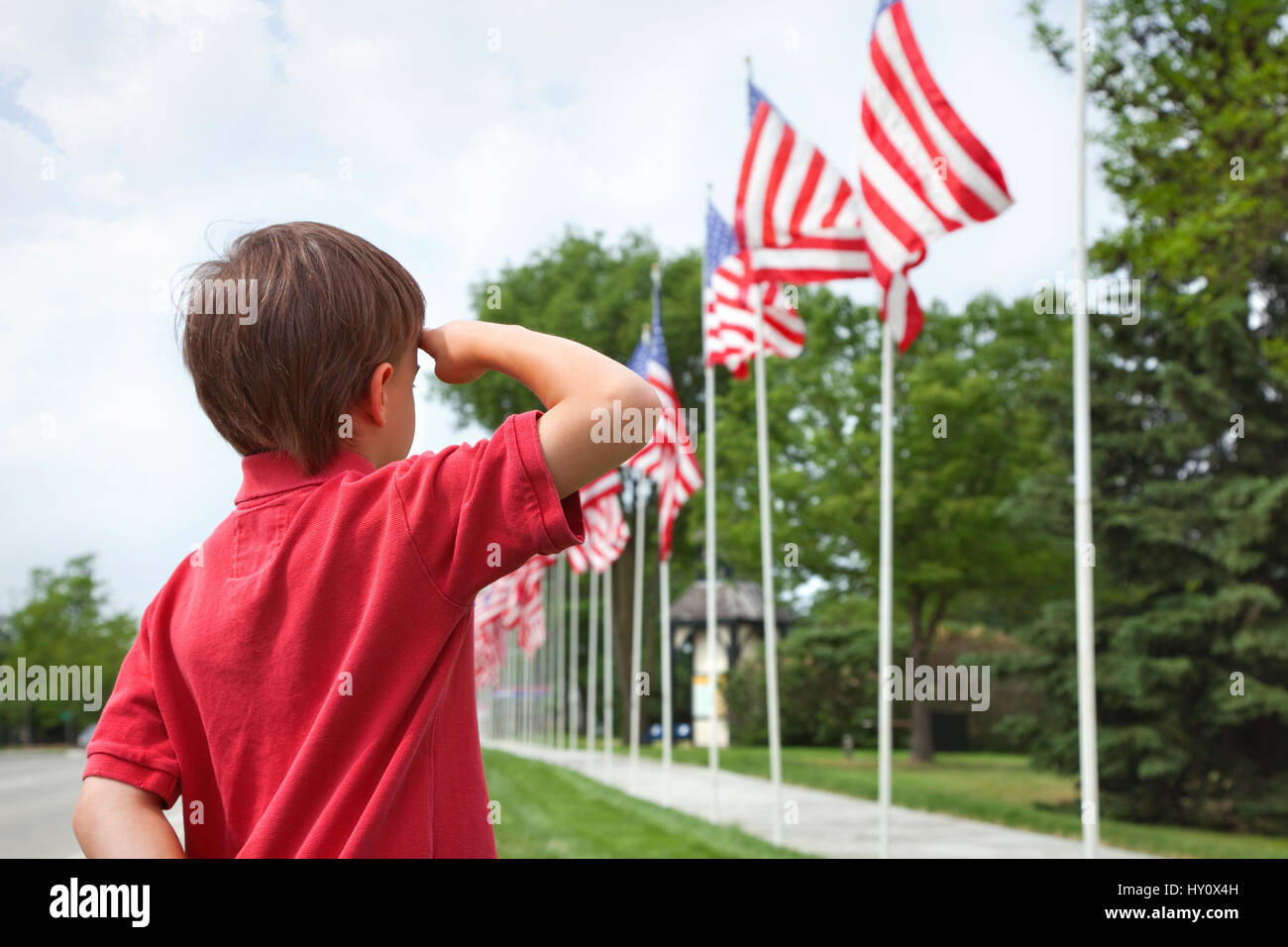 Un jeune garçon salue les drapeaux de Memorial Day affiche ainsi une petite ville street Banque D'Images