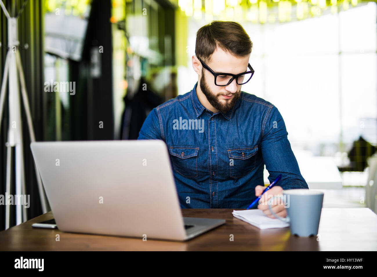 Student taking notes de son nouvel ordinateur portable lors de la navigation sur Internet avec son café du matin Banque D'Images