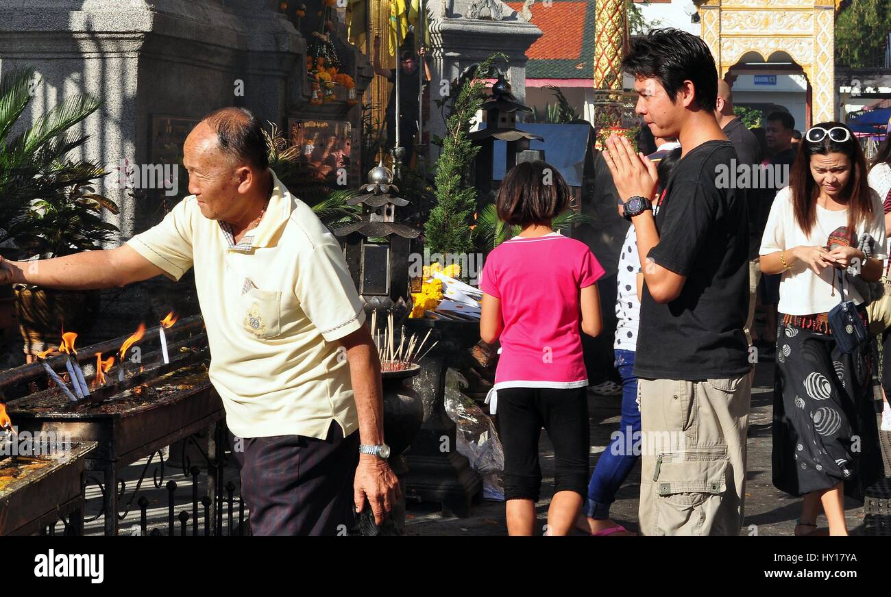 Lamphun, Thaïlande - 28 décembre 2012 : Thai man, les mains jointes dans la prière, des montres comme un autre s'allume un cierge à Wat Phra That Haripunchai Maha Viham Banque D'Images