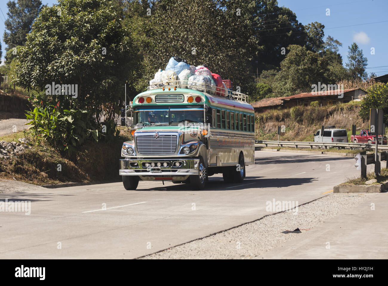 Gros autobus conduire sur route de montagne rurale au Guatemala, en Amérique centrale. Le bus est rempli de personnes et de biens sur le toit. Ces bus sont connus Banque D'Images