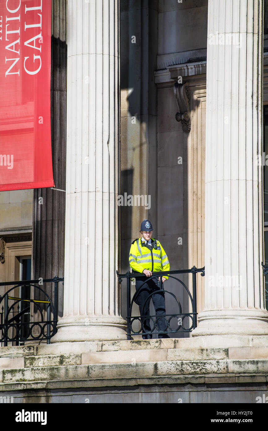 Un agent de police métropolitaine sondages Trafalgar Square à partir d'un balcon à la National Gallery de Londres, en Angleterre. Banque D'Images