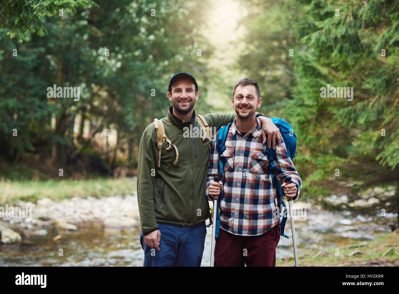 Deux randonneurs souriant debout près de rivière dans une forêt Banque D'Images