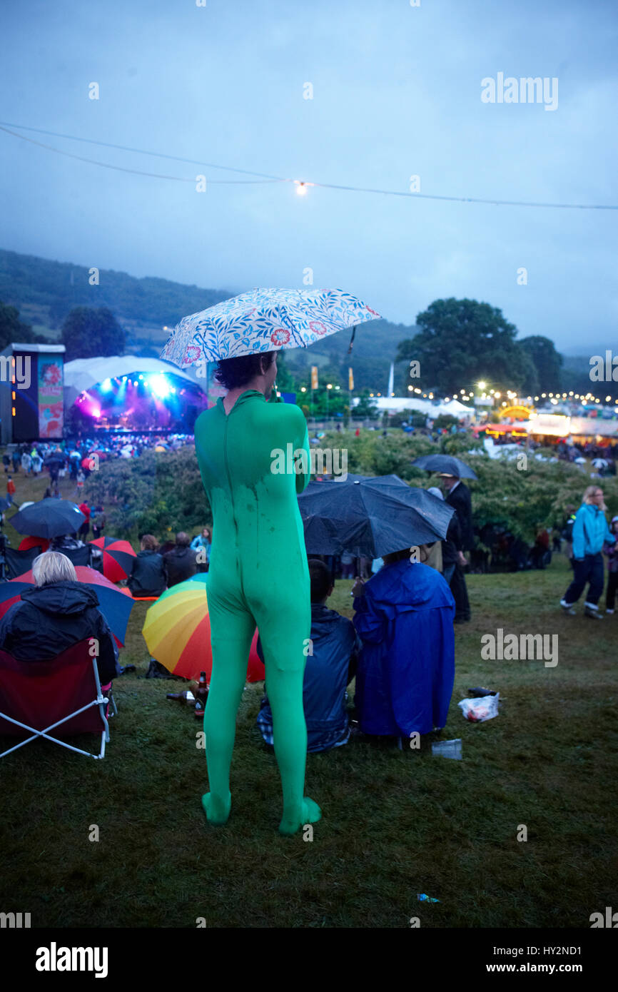 Homme debout dans une foule portant un collant vert avec un parapluie en regardant des groupes live, le Green Man Festival, au Pays de Galles. Banque D'Images