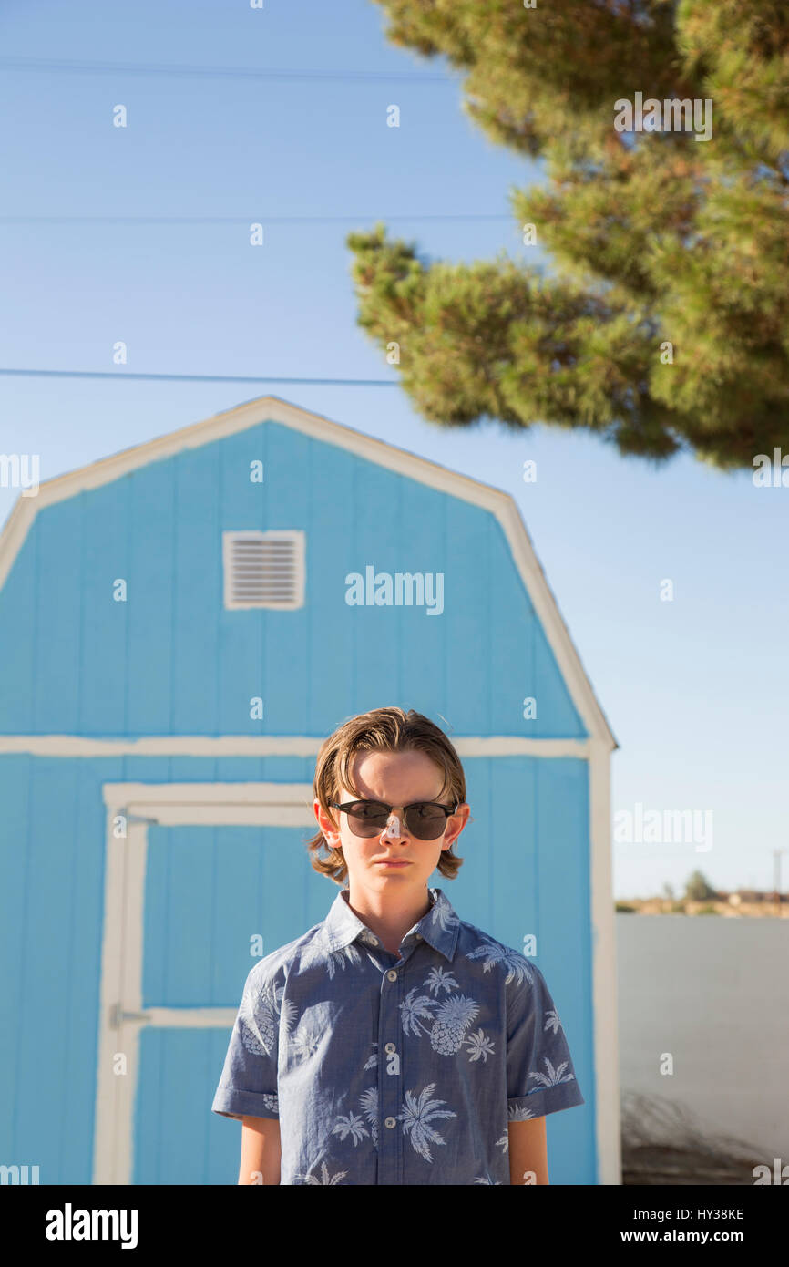 États-unis, Californie, Boy (14-15) wearing sunglasses standing in front of blue barn Banque D'Images