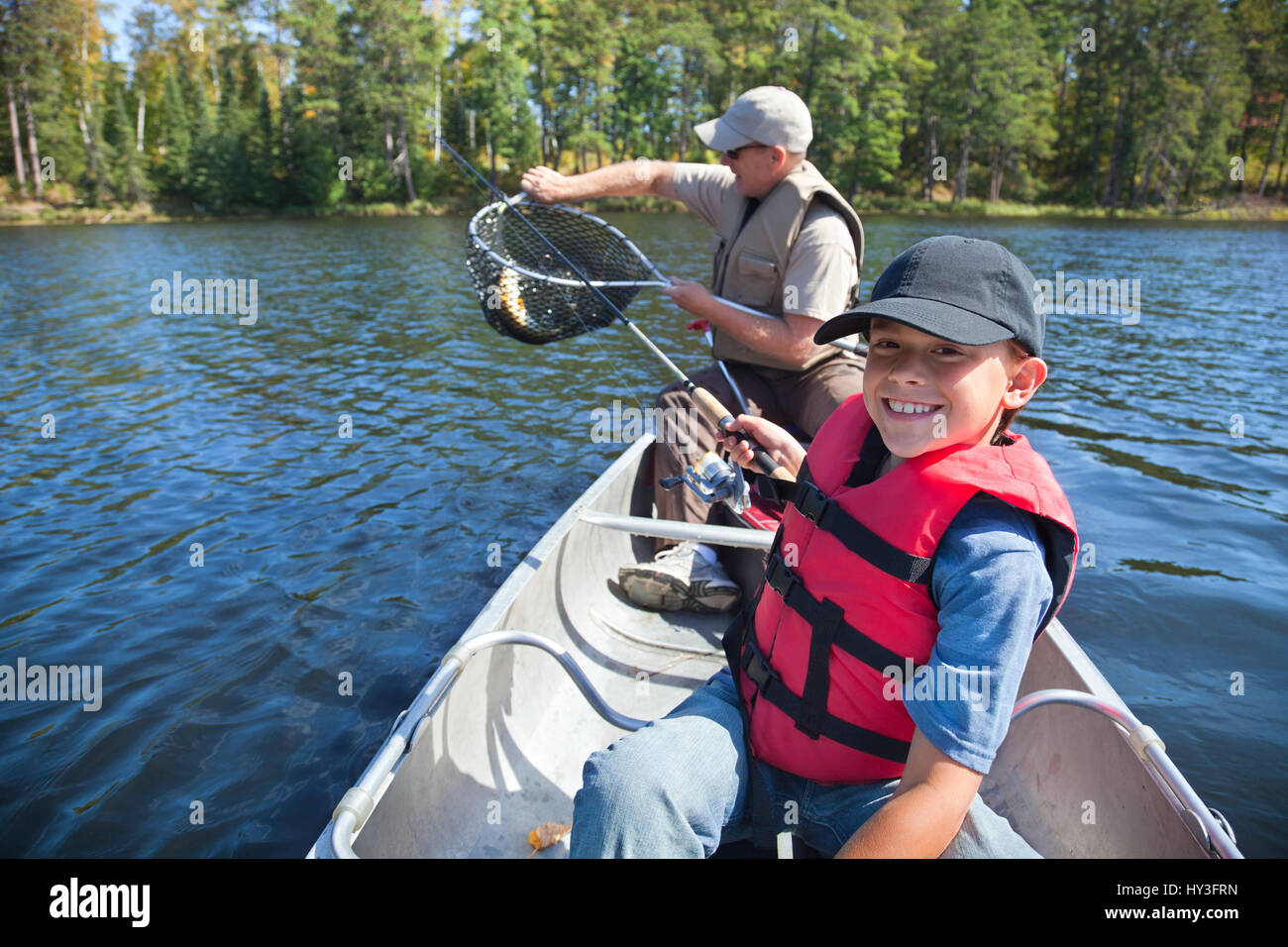Jeune garçon sourit tandis que son père pêcheur prend le poisson du filet Banque D'Images