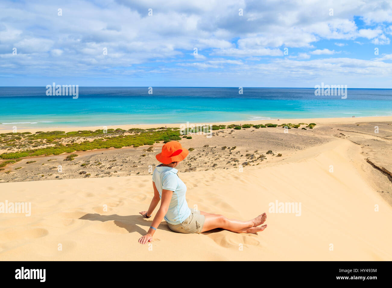 Jeune Femme au chapeau orange assis sur une dune de sable à la plage de Sotavento de Jandia sur peninsula, Fuerteventura, Îles Canaries, Espagne Banque D'Images