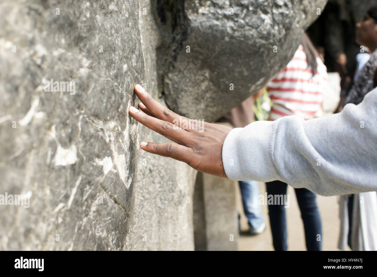 Un pèlerin touche le mur de pierre de la grotte de Massabielle, à Lourdes, France, la visite d'un printemps que saint est réputé pour avoir des propriétés de guérison Banque D'Images