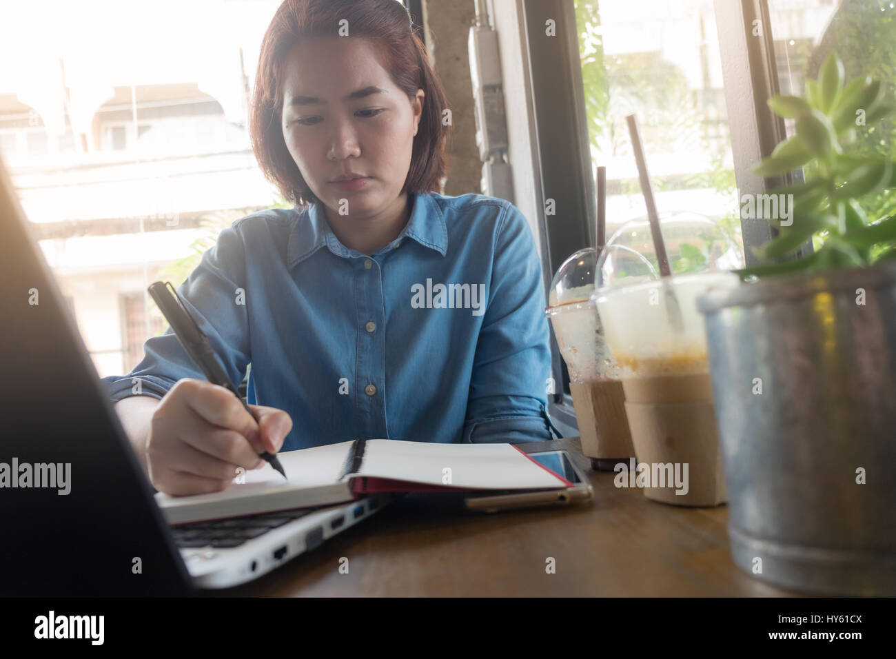 Young Asian woman hipster journal sur ordinateur portable avec émotion grave dans un coffee shop. Offres d'activité starup concept Banque D'Images