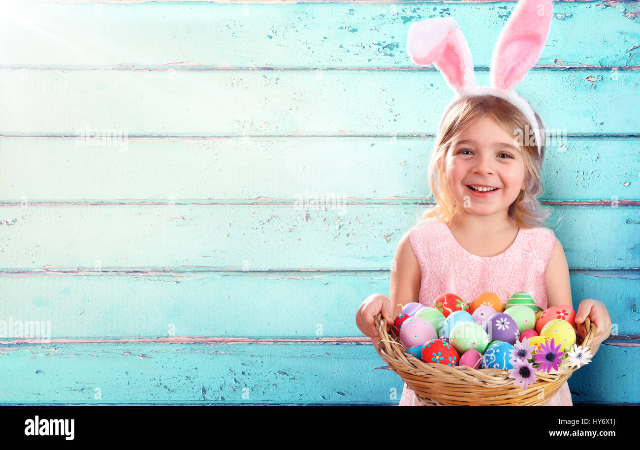 Pâques - Petite fille avec panier d'oeufs et oreilles de lapin et fond en bois bleu Banque D'Images