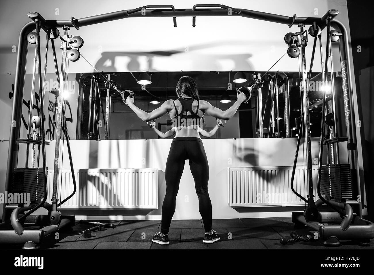 Woman flexing muscles sur le câble de la machine en salle de sport. L'exercice sur biceps. Vue arrière Banque D'Images