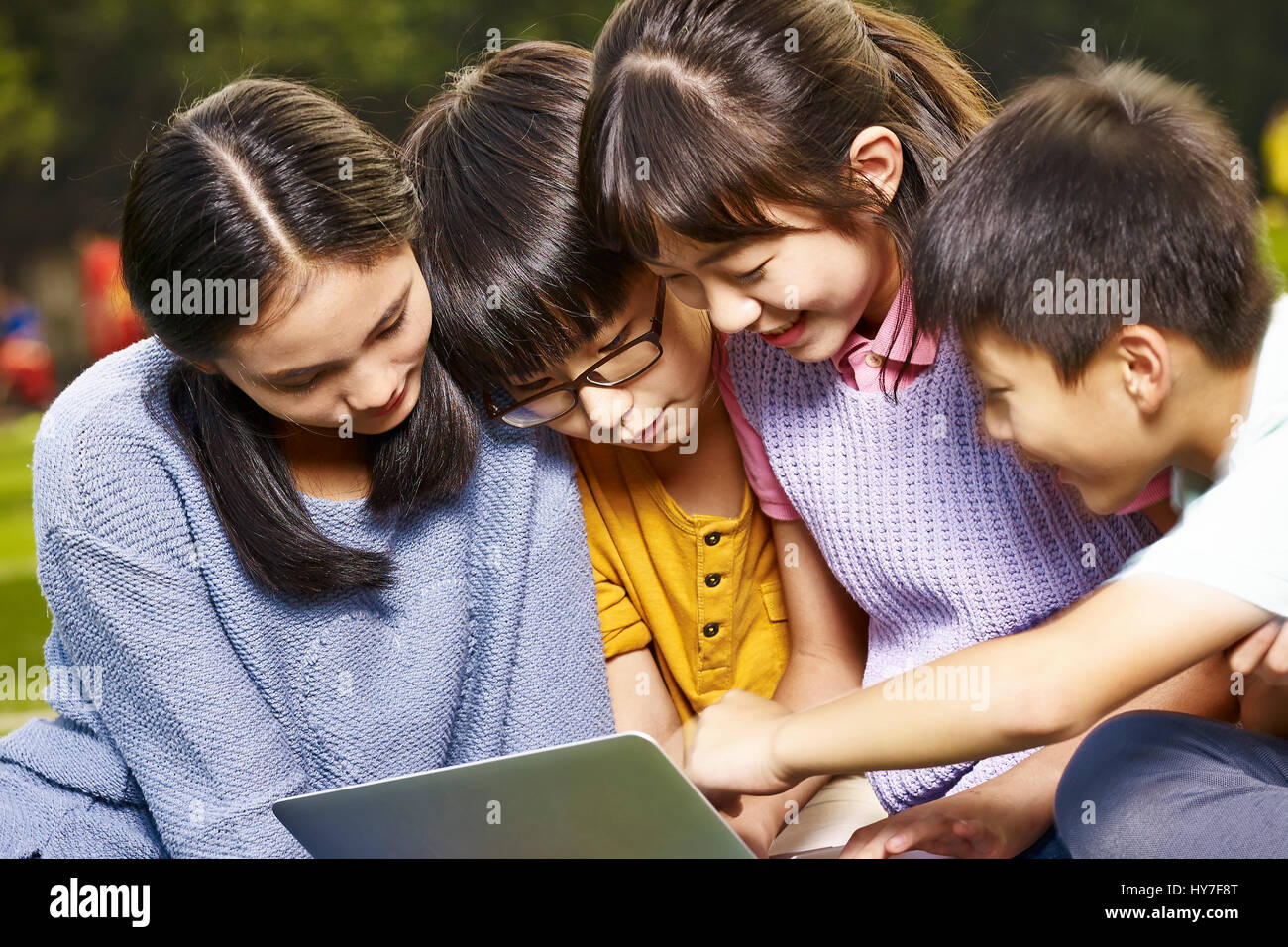 Des écoliers et écolières du primaire asiatique en utilisant un ordinateur portable ensemble à l'extérieur. Banque D'Images