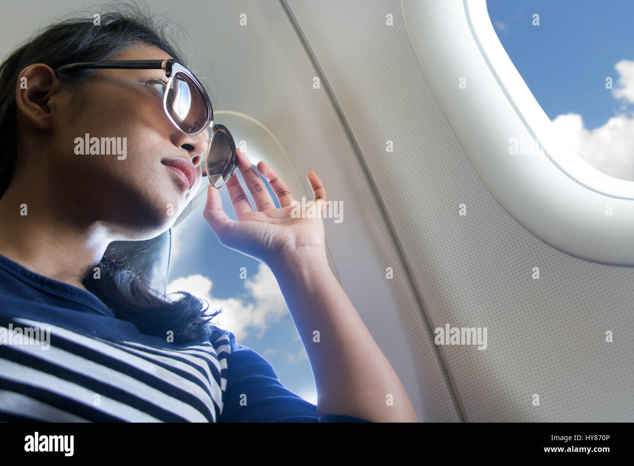Avec des lunettes de soleil femme regarde par la fenêtre d'un avion volant.  Les jeunes passagers voyagent en avion, à regarder le ciel Photo Stock -  Alamy
