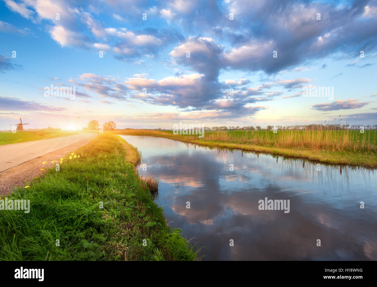 Paysage de printemps. Bleu Couleur ciel nuageux reflète dans l'eau, l'herbe verte et jaune soleil, route et moulin au lever du soleil en Pays-Bas. Amazing colorf Banque D'Images