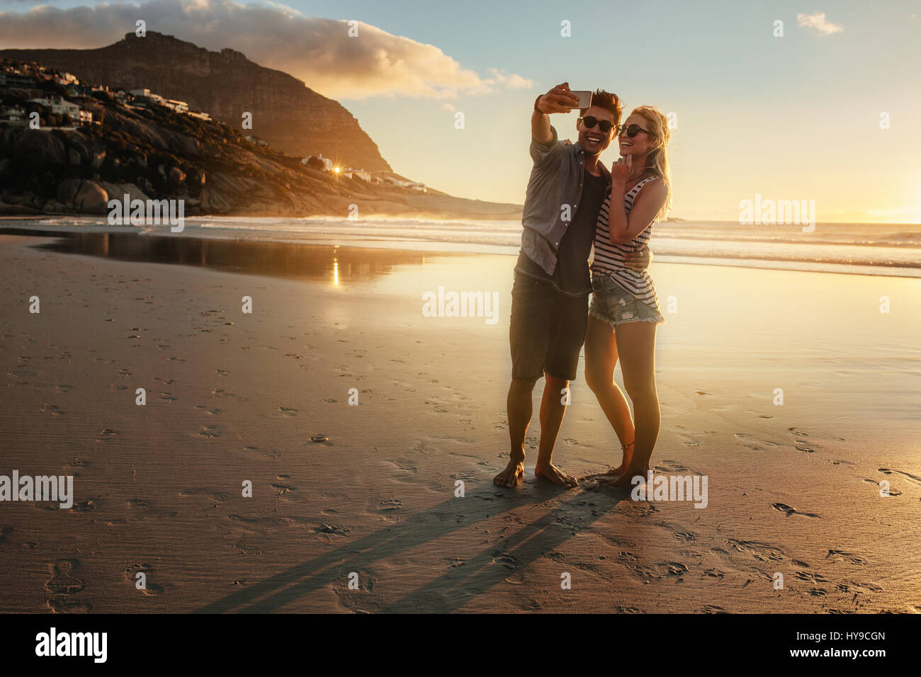 Couple romantique à la plage selfies. Jeune homme et femme sur la mer en tenant avec selfies téléphone mobile pendant le coucher du soleil. Banque D'Images