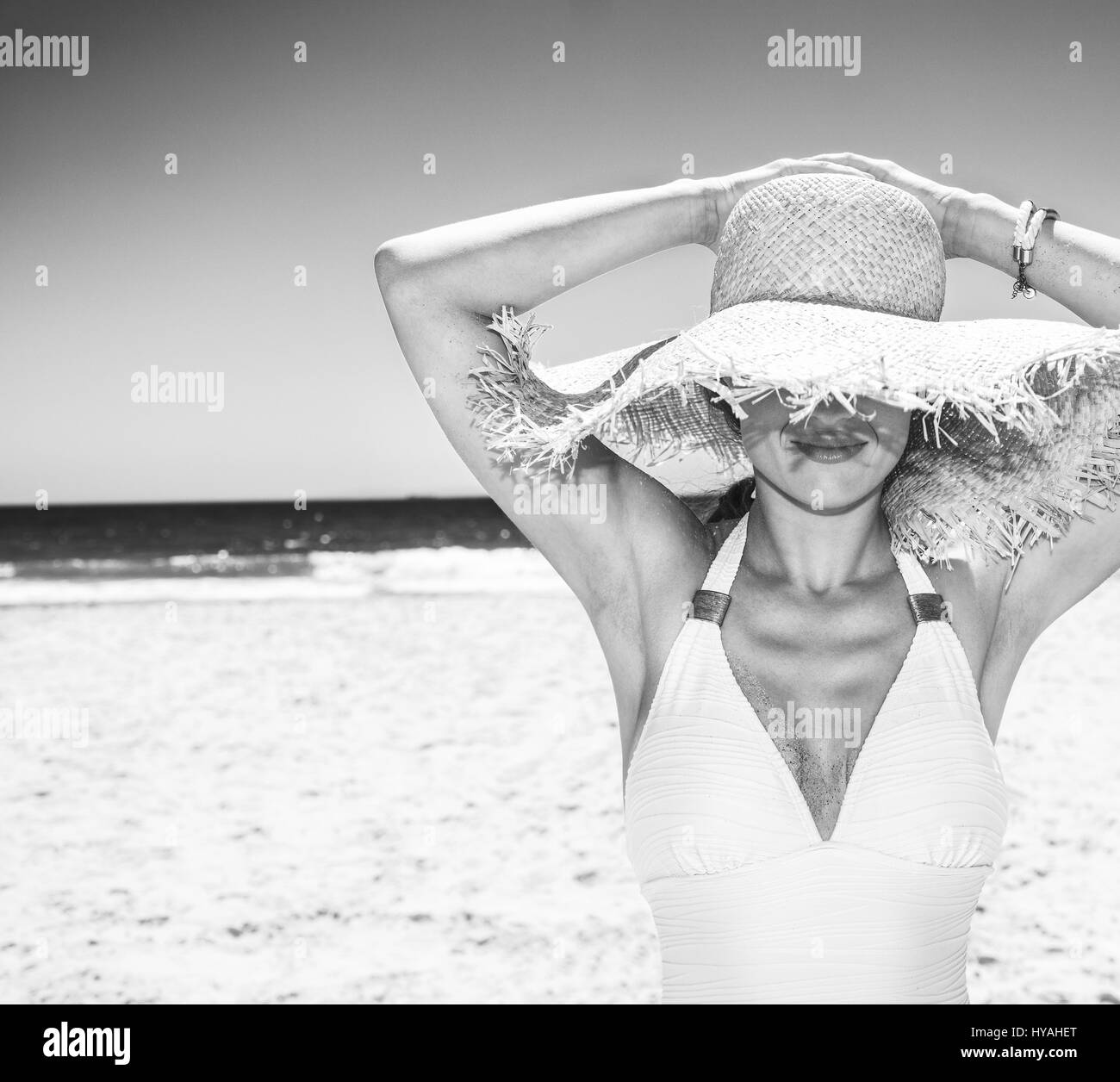 La position de sable blanc mer bleu paradis. Femme en maillot blanc caché sous grand chapeau de paille à sandy beach sur une journée ensoleillée Banque D'Images
