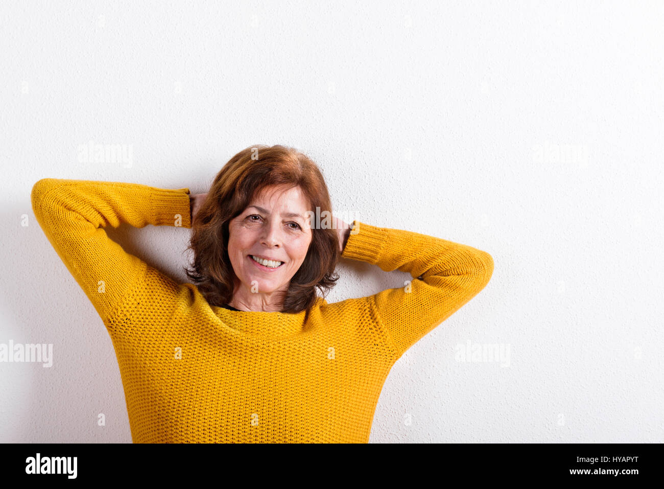 Senior woman in pull en laine jaune, studio shot. Banque D'Images