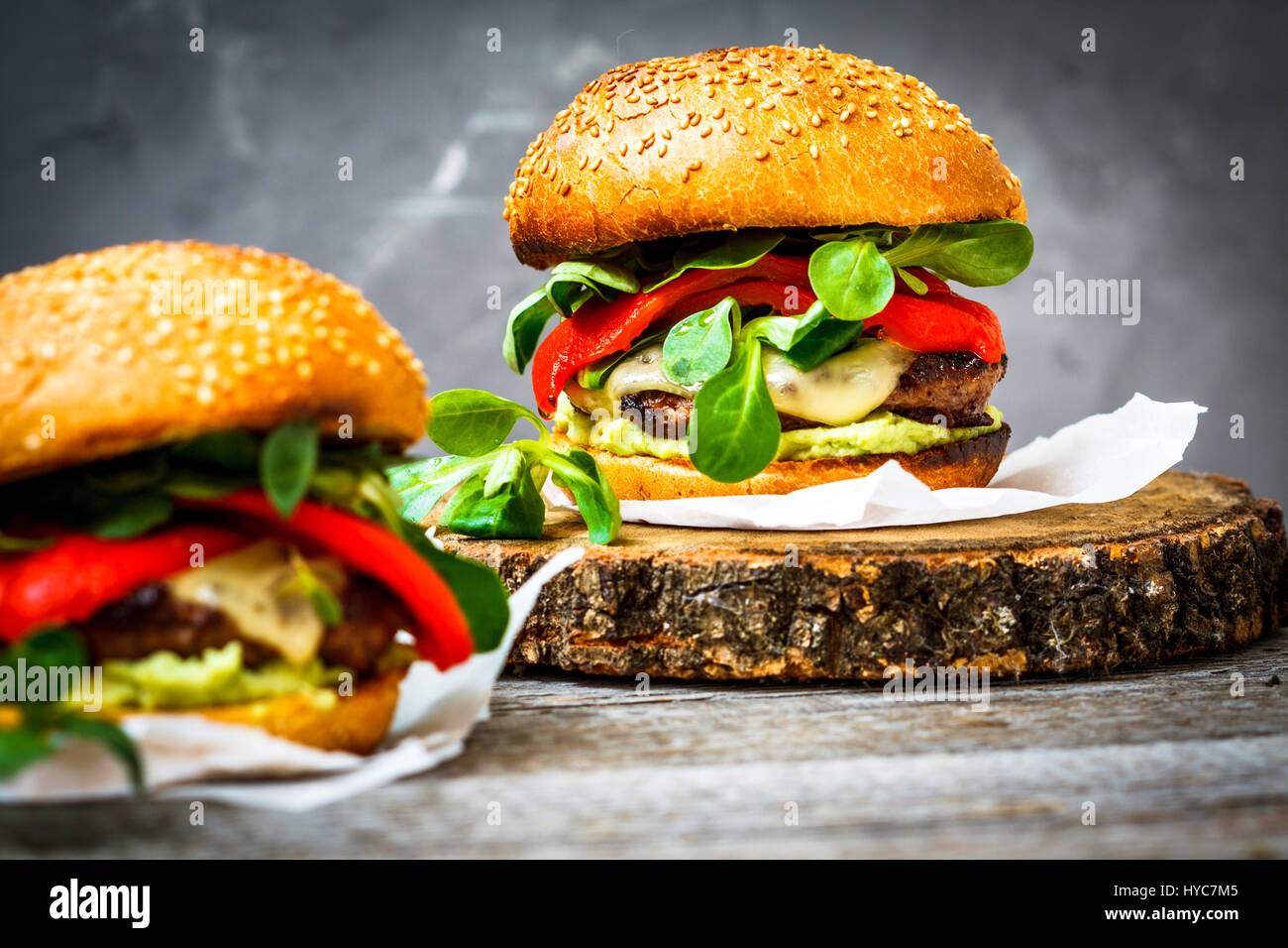 Tasty burger de bœuf grillé avec du fromage, de guacamole et de poivrons marinés. Fond sombre, brown paper, support en bois. Banque D'Images