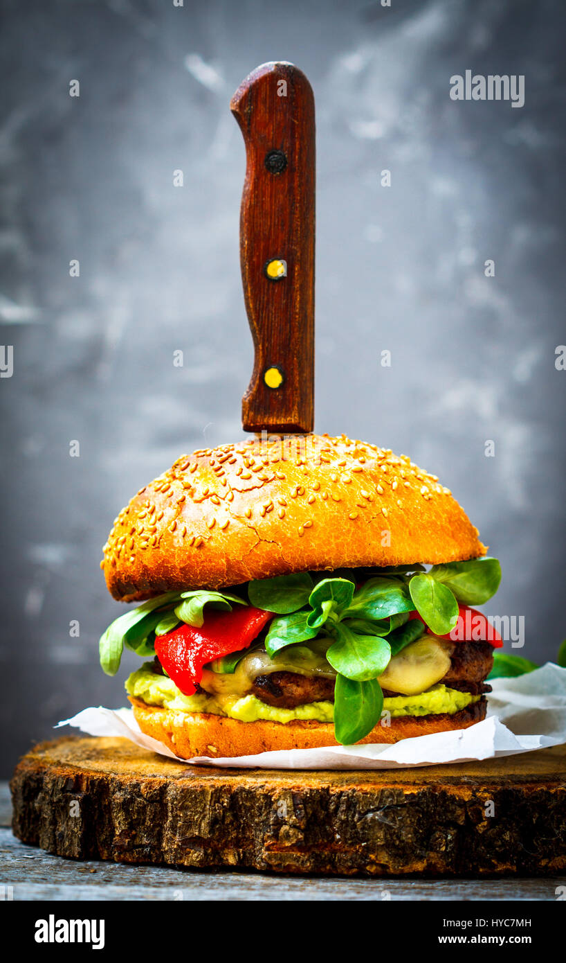 Tasty burger de bœuf grillé avec du fromage, de guacamole et de poivrons marinés. Fond sombre, brown paper, support en bois. Banque D'Images