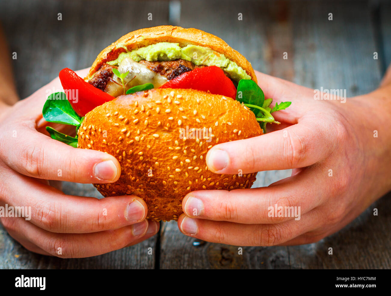 Tasty burger de bœuf grillé avec du fromage, de la guacamole et poivrons marinés entre les mains de l'homme. Banque D'Images