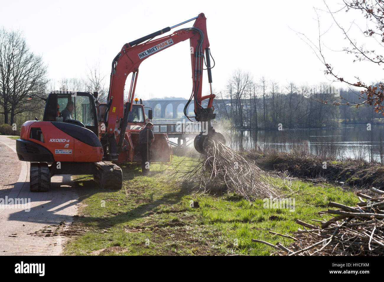 Excavatrice KUBOTA KX080-4/manutentionnaire ascenseurs tree branches vers le déchiquetage des résidus verts en tant que travailleurs de la machine gérer une zone de forêt Banque D'Images