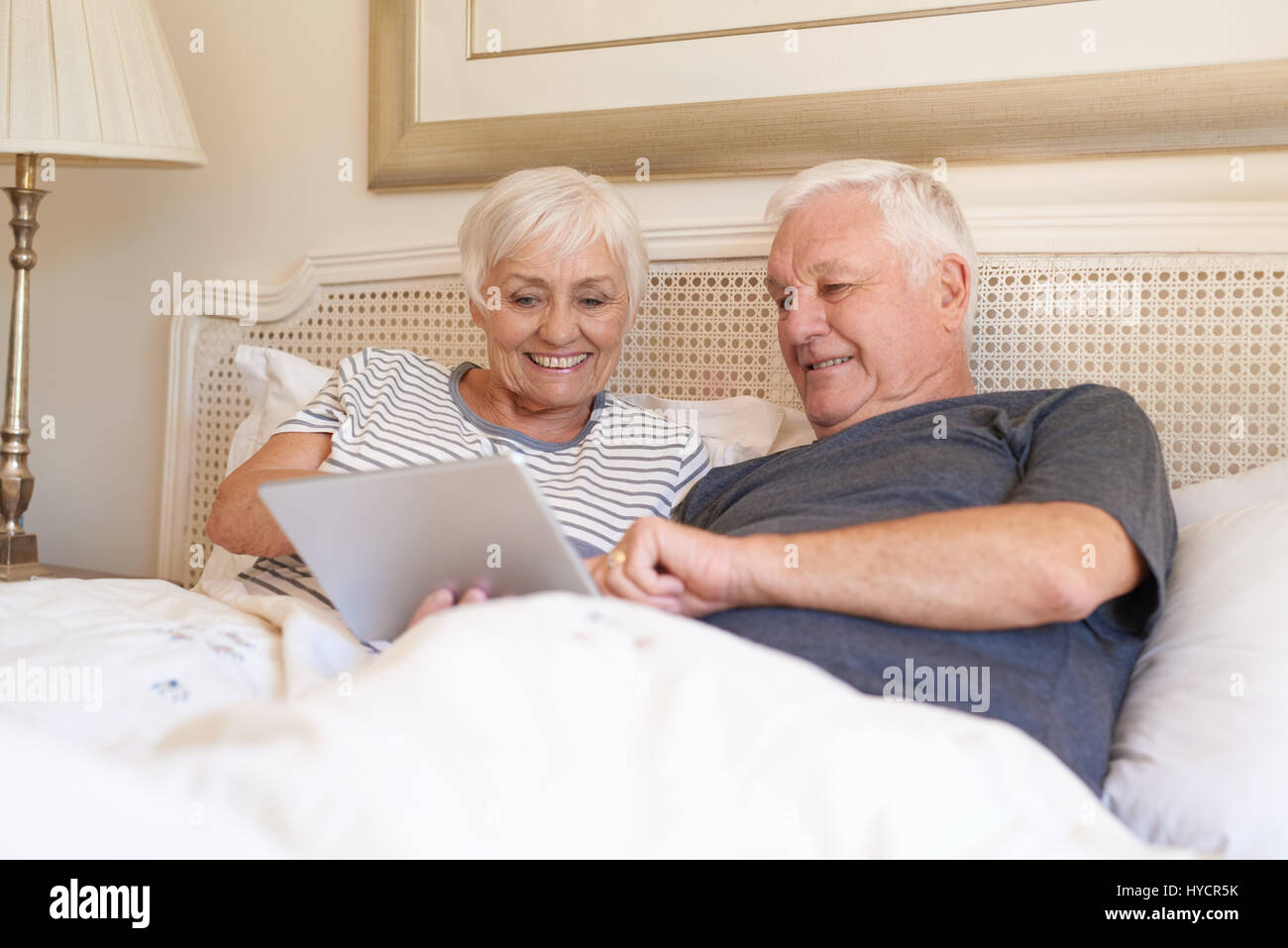 Smiling seniors à l'aide d'une tablette numérique together in bed Banque D'Images