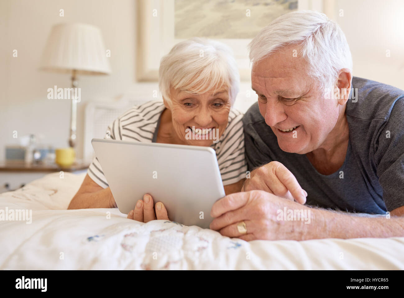 Smiling senior couple using a digital tablet together in bed Banque D'Images