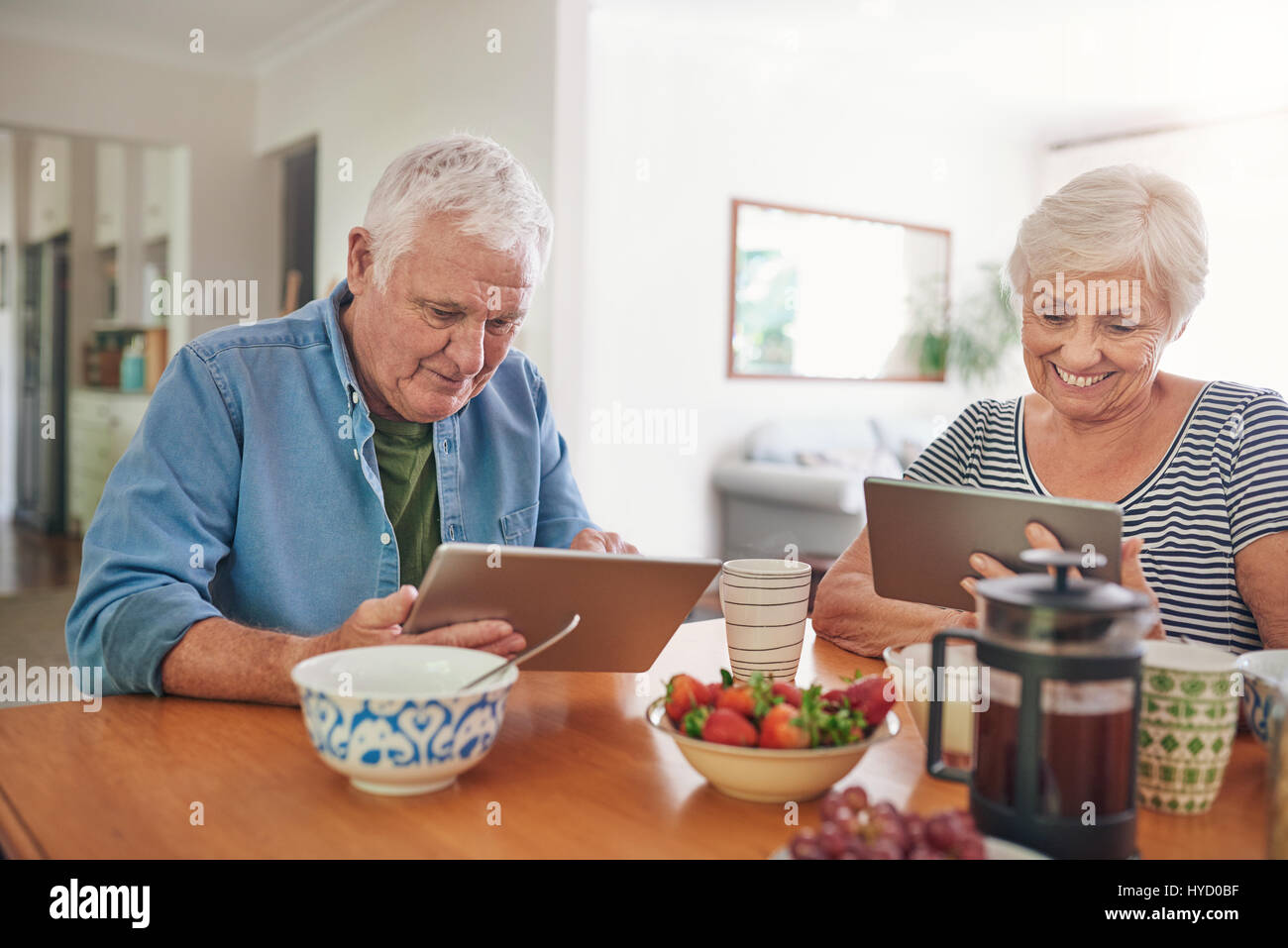 Smiling seniors à l'aide de tablettes numériques pendant le petit-déjeuner à la maison Banque D'Images