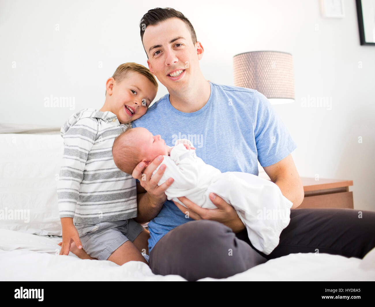 Père transportant sa fille (0-1 mois) et assis sur le lit avec son fils  (4-5 Photo Stock - Alamy