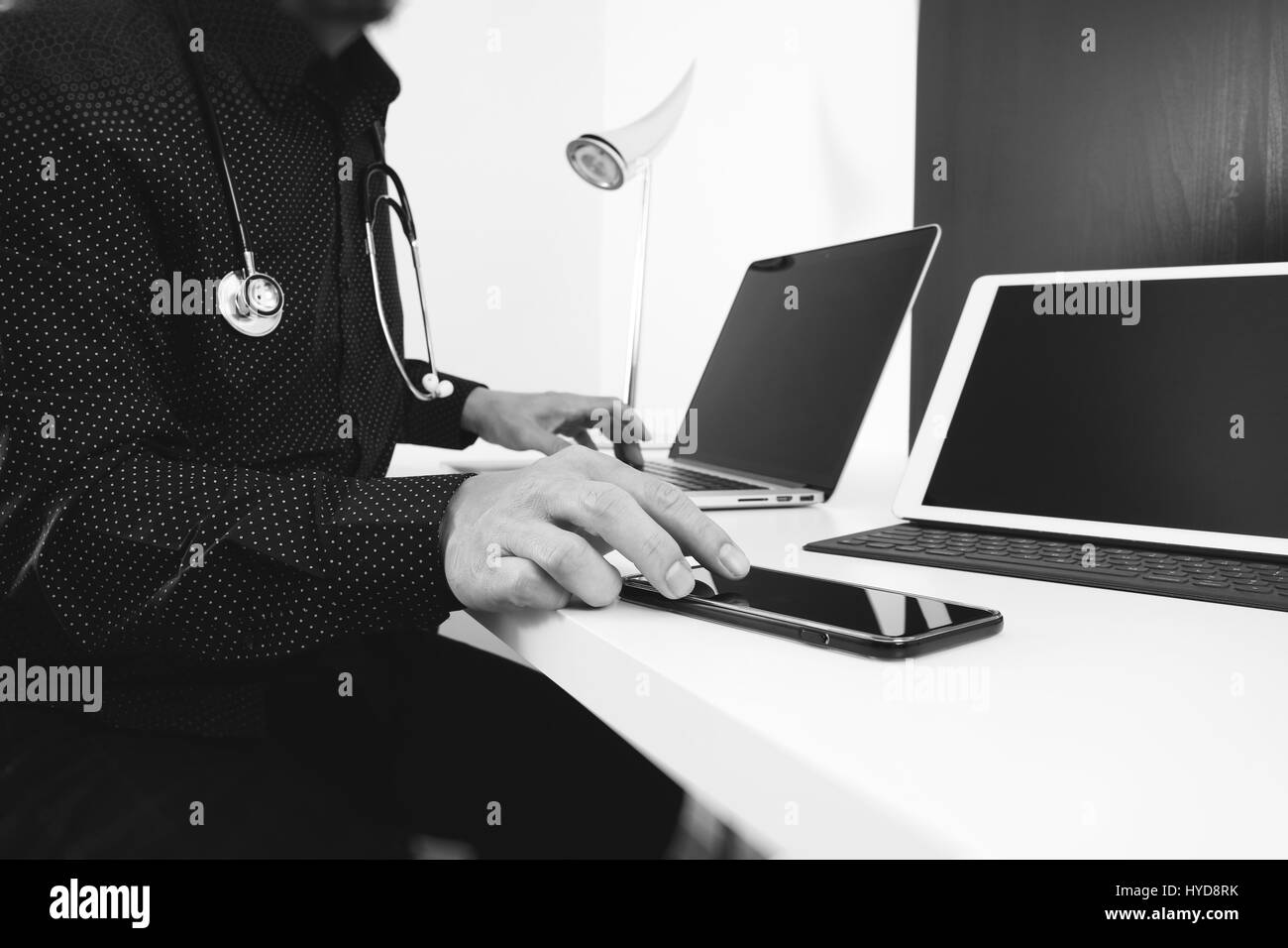 Smart médecin avec smart phone et tablette numérique et ordinateur portable et stéthoscope sur bois bureau dans un bureau moderne, noir et blanc Banque D'Images