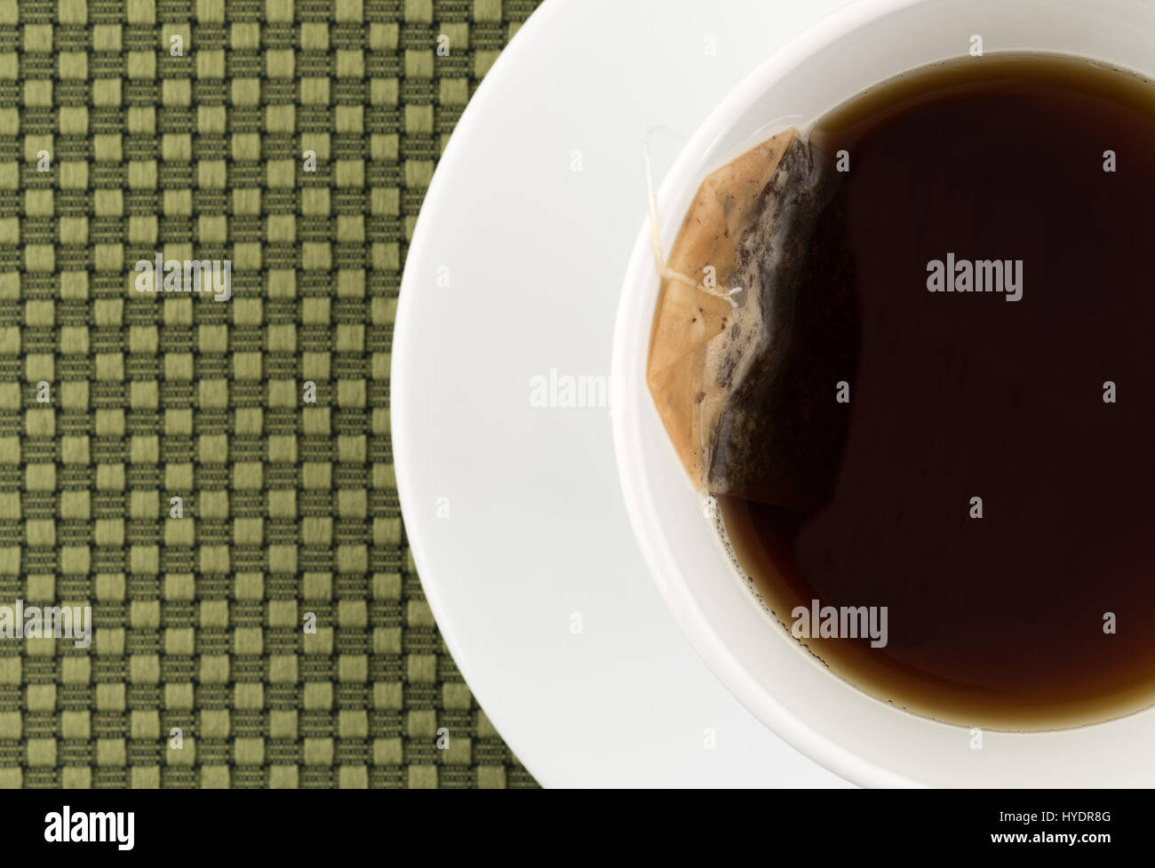 Haut de page Fermer la vue d'une tasse et soucoupe de thé noir décaféiné avec un sachet de thé dans le liquide sur un endroit vert mat. Banque D'Images
