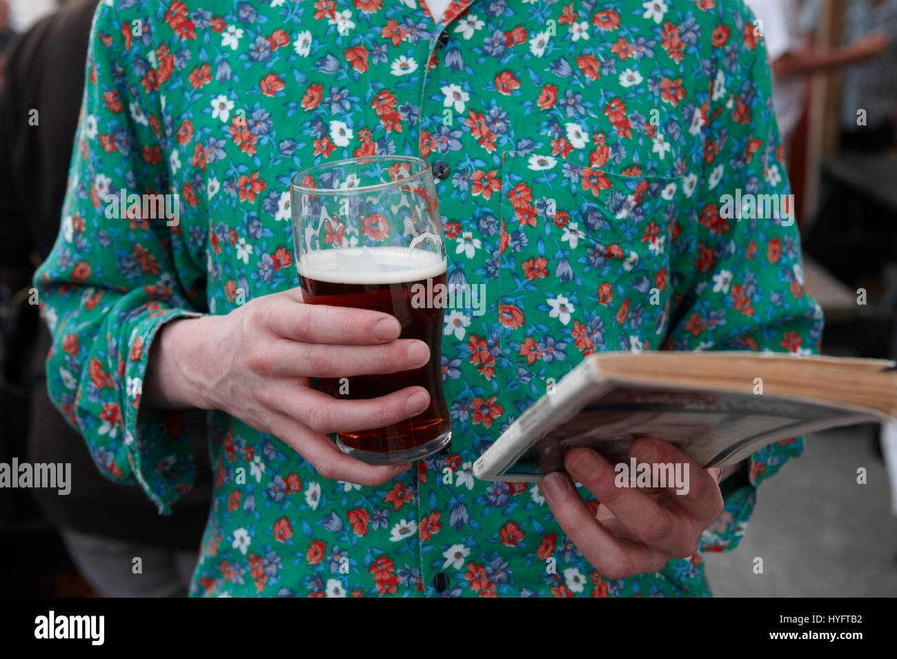 Un homme portant un haut fleuri vert la lecture d'un livre, la tenue d'une pinte au Festival littéraire, Carmarthen, pays de Galles, Royaume-Uni Banque D'Images