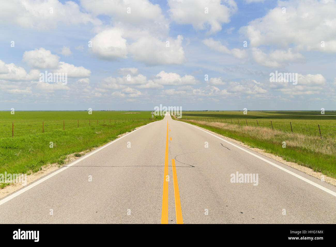 Road en passant par la région de Flint Hills au Kansas, avec les pâturages verts de chaque côté, et ciel bleu avec quelques nuages blancs. Banque D'Images
