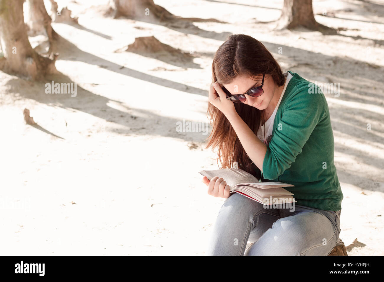 Belle jeune femme brune portant des lunettes de soleil et pull vert est  emporté par la lecture d'un livre dans le parc Photo Stock - Alamy