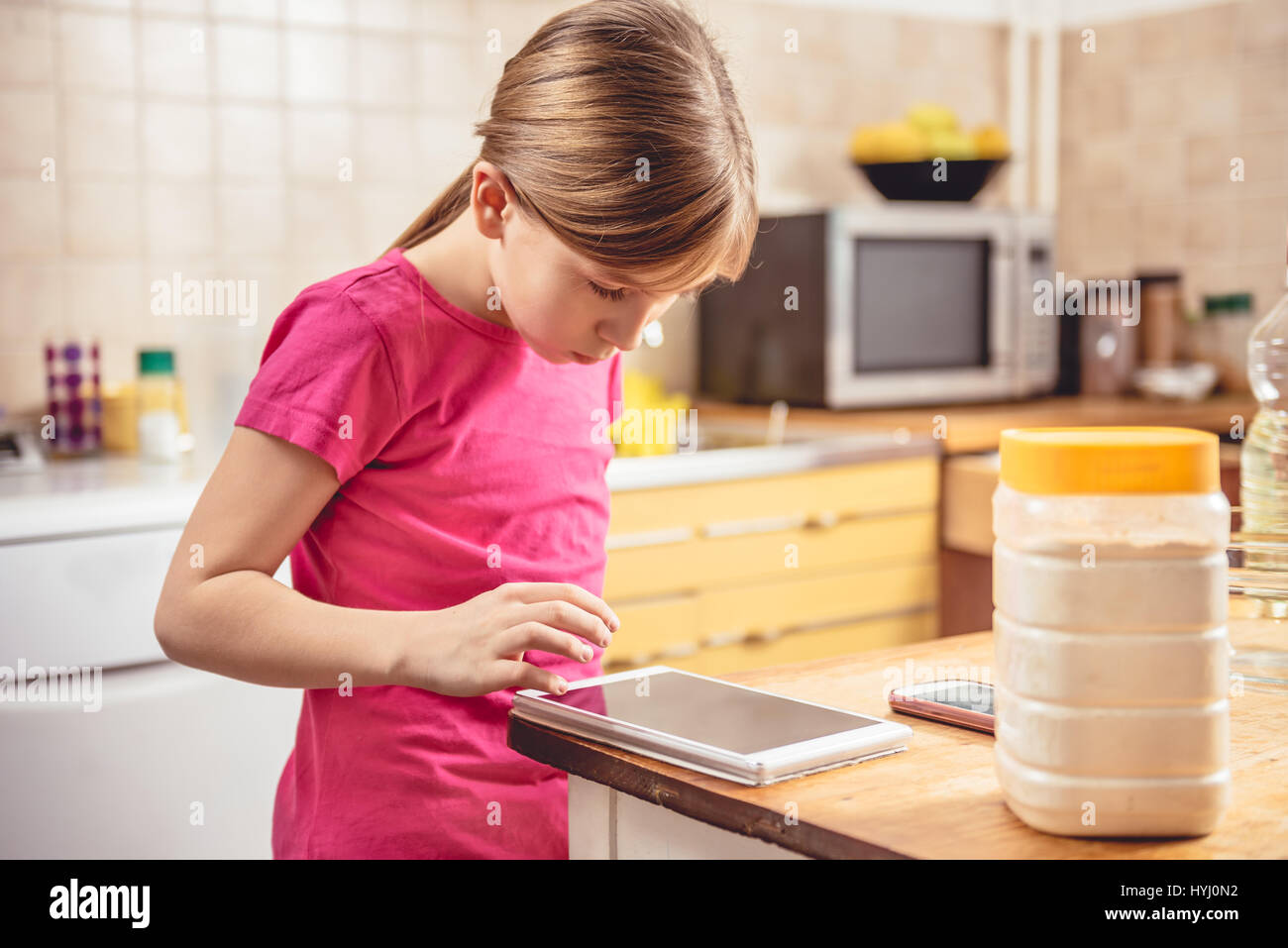 Little girl wearing pink shirt à l'aide de tablette dans la cuisine Banque D'Images
