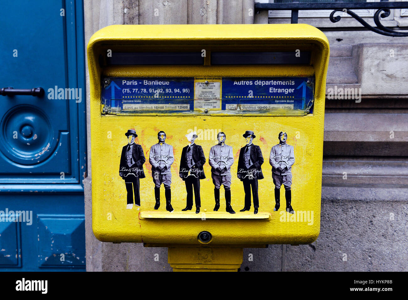 Caisse postale française jaune à Paris ornée d'une œuvre d'art de rue au pochoir représentant des personnages avec des chapeaux et des manteaux vintage Banque D'Images