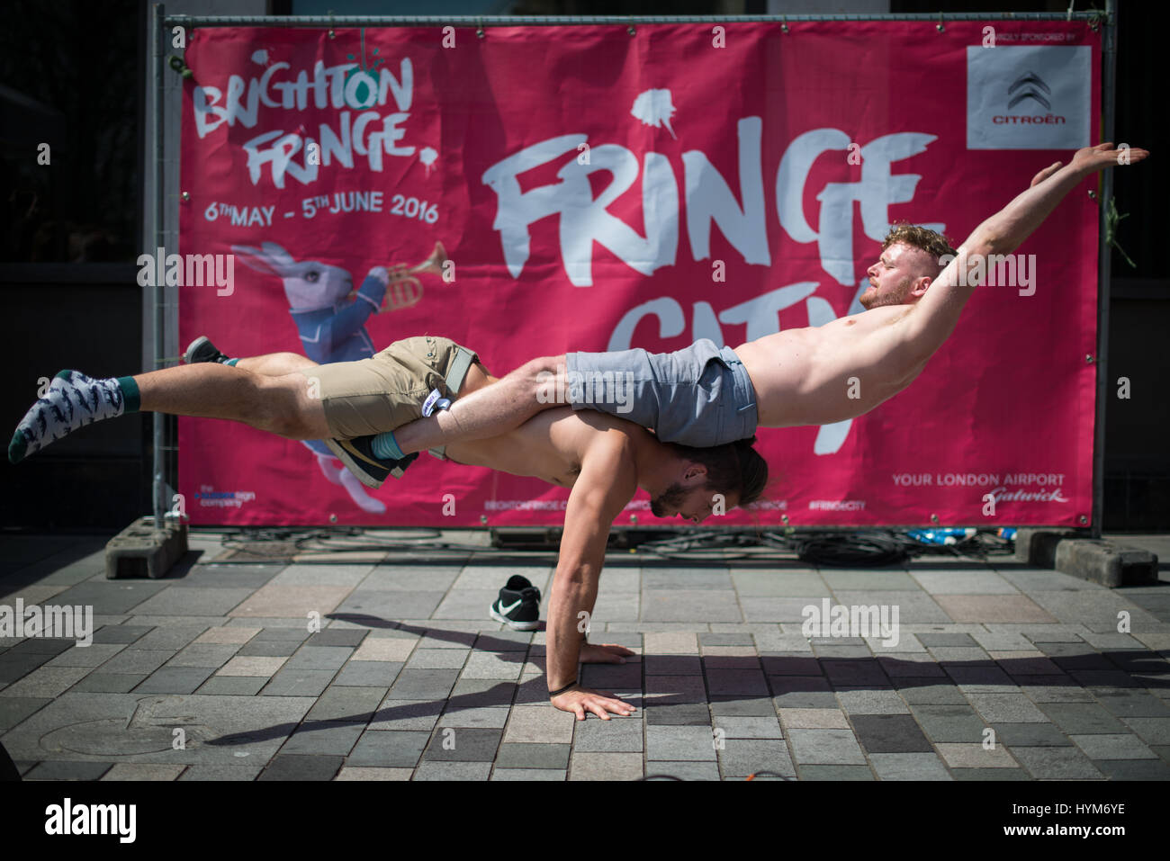 Un mâle acrobat effectue un atr tandis que son ami se repose sur son dos pendant une performance de rue au Fringe Brighton à Brighton, East Sussex, UK. Banque D'Images