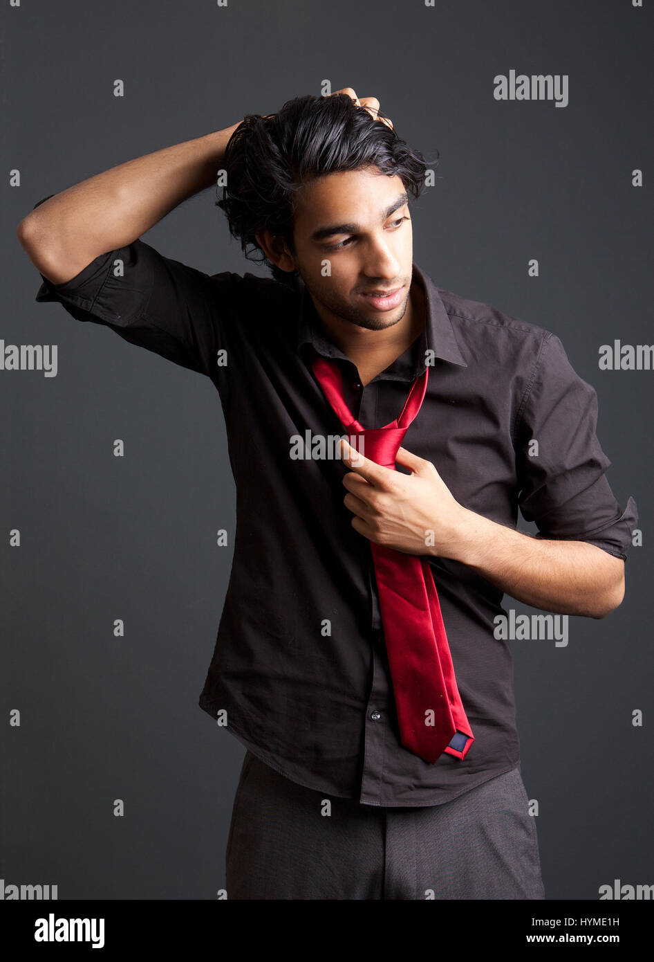Portrait d'un jeune homme à la chemise noire et cravate rouge posant avec  la main dans les cheveux à l'arrière-plan gris Photo Stock - Alamy