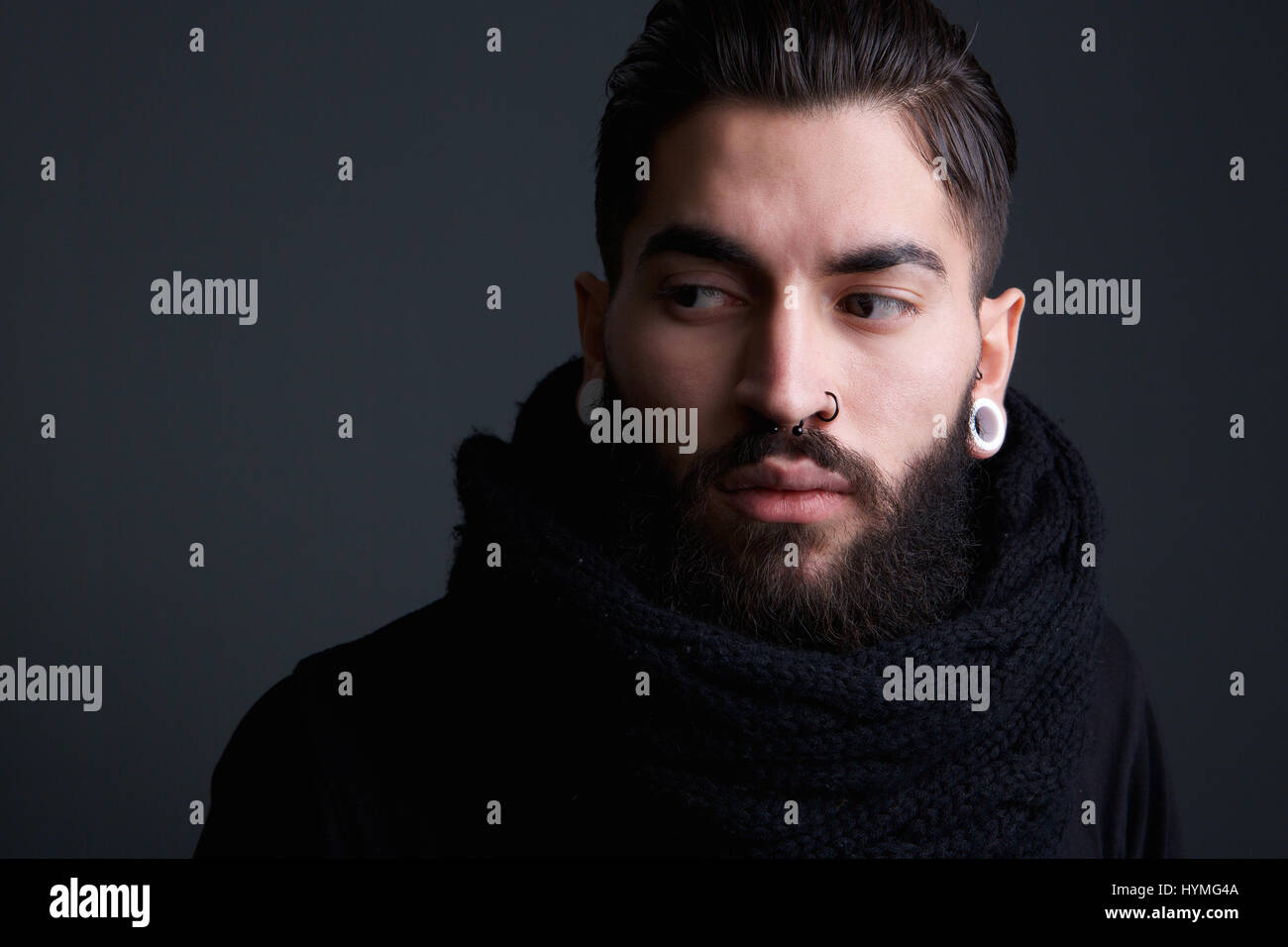 Portrait d'un jeune homme moderne edgy avec barbe et de piercings posant sur fond gris Banque D'Images