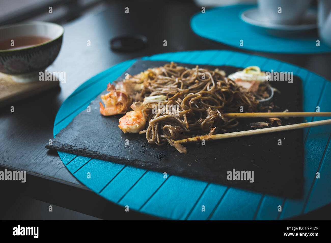 Nouilles de sarrasin aux crevettes et les copeaux de thon avec la sauce sur la plaque noire. Arrière-plan de l'alimentation asiatique. Concept de l'alimentation. Restaurant place avec table en bois. Flare copie espace pour texte, design Banque D'Images