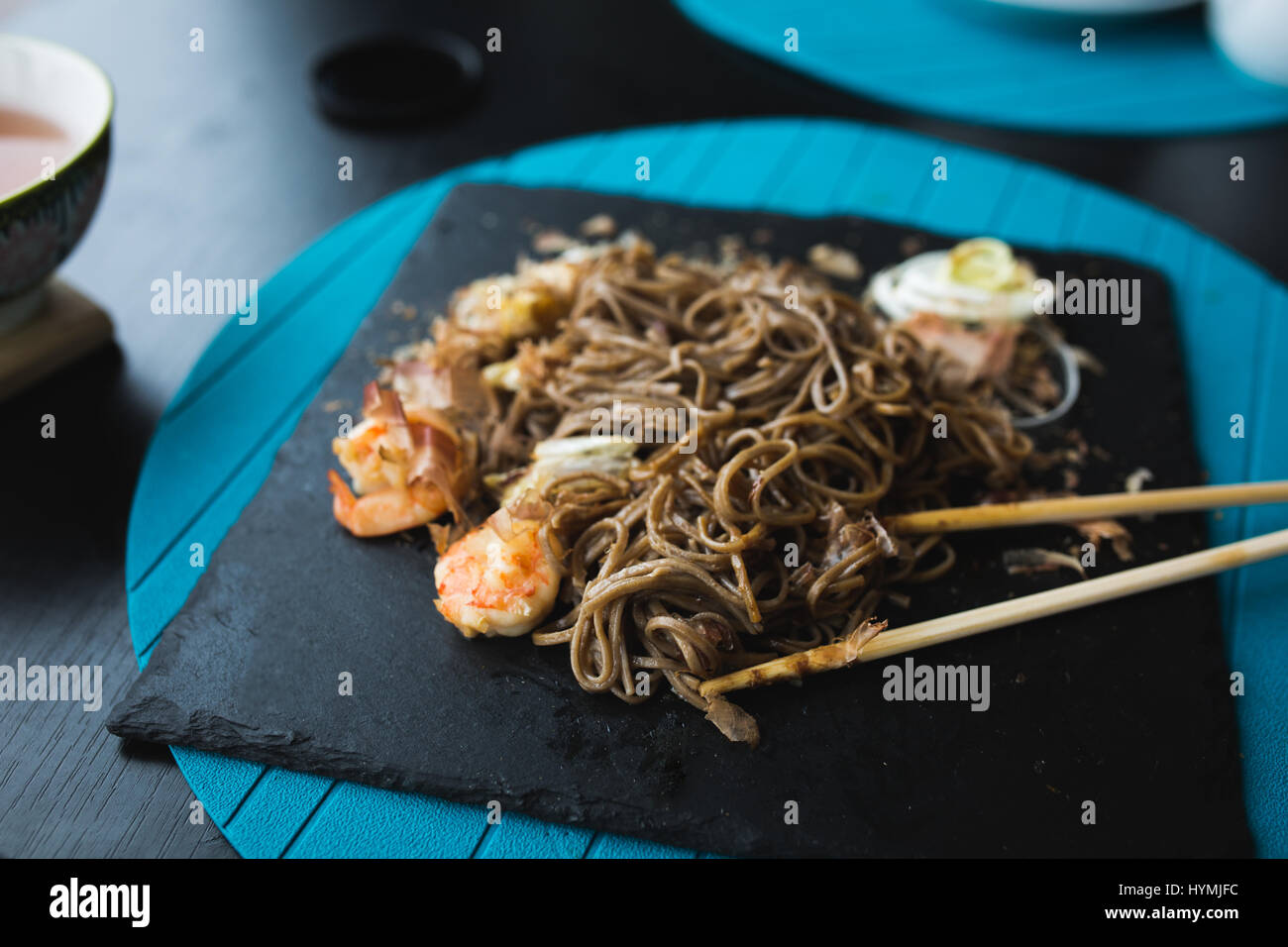 Nouilles de sarrasin aux crevettes et les copeaux de thon avec la sauce sur la plaque noire. Arrière-plan de l'alimentation asiatique. Concept de l'alimentation. Restaurant place avec table en bois. Flare copie espace pour texte, design Banque D'Images