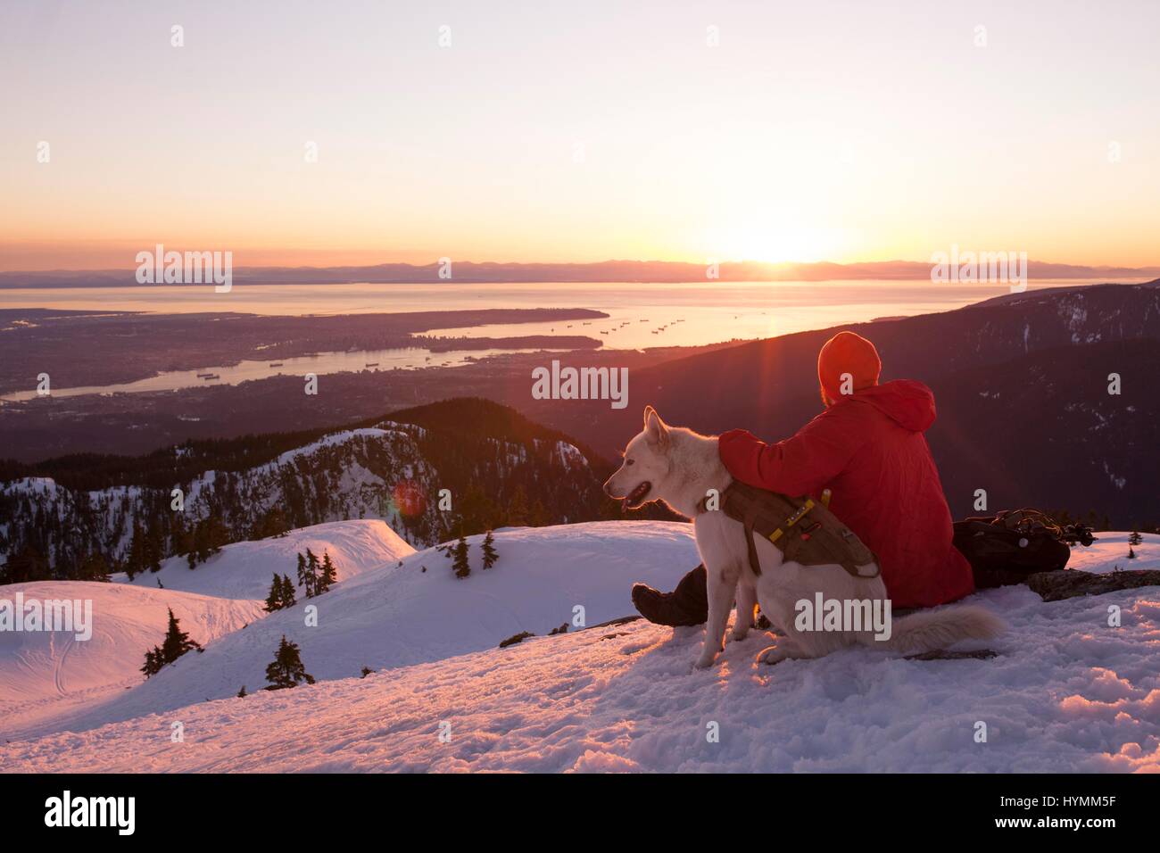 L'homme et son chien regardant le coucher du soleil avec vue sur l'océan depuis le sommet de la montagne en hiver, Vancouver, Whistler, British Columbia, Canada Banque D'Images