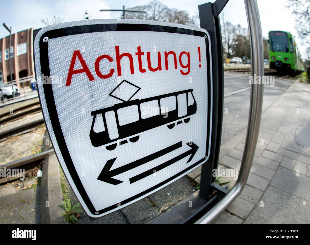 Un tramway s'approche d'un passage à niveau, où un signe avec le mot  "Achtung" ("attention") met en garde les piétons à regarder des deux côtés  avant de traverser les voies à Hanovre,