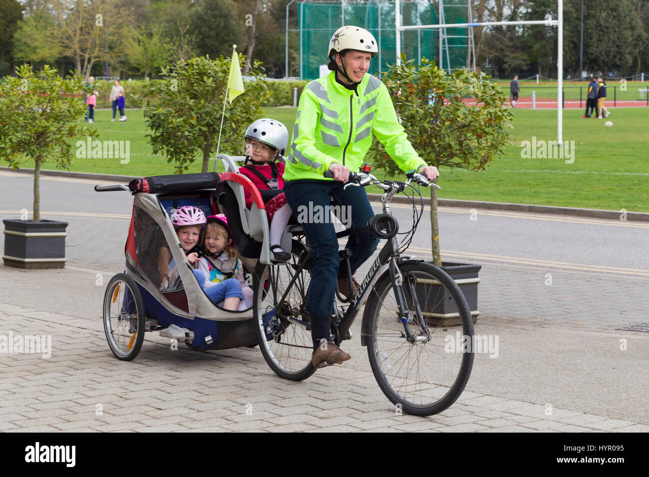 Cycliste femme sur Vélo / Vélo avec  + 3 enfants ; coopération avec siège enfant pilote casque & cycle remorquage remorque Chariot avec 2 / 2 enfants avec un casque. UK. Banque D'Images