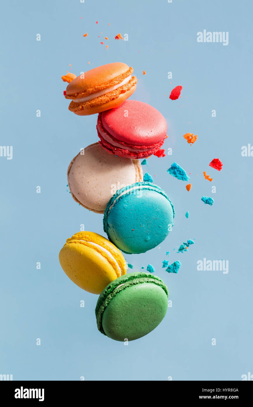 Différents types de macarons dans motion relevant sur fond bleu clair. Doux et coloré qui tombent ou qui volent les macarons français en mouvement. Banque D'Images
