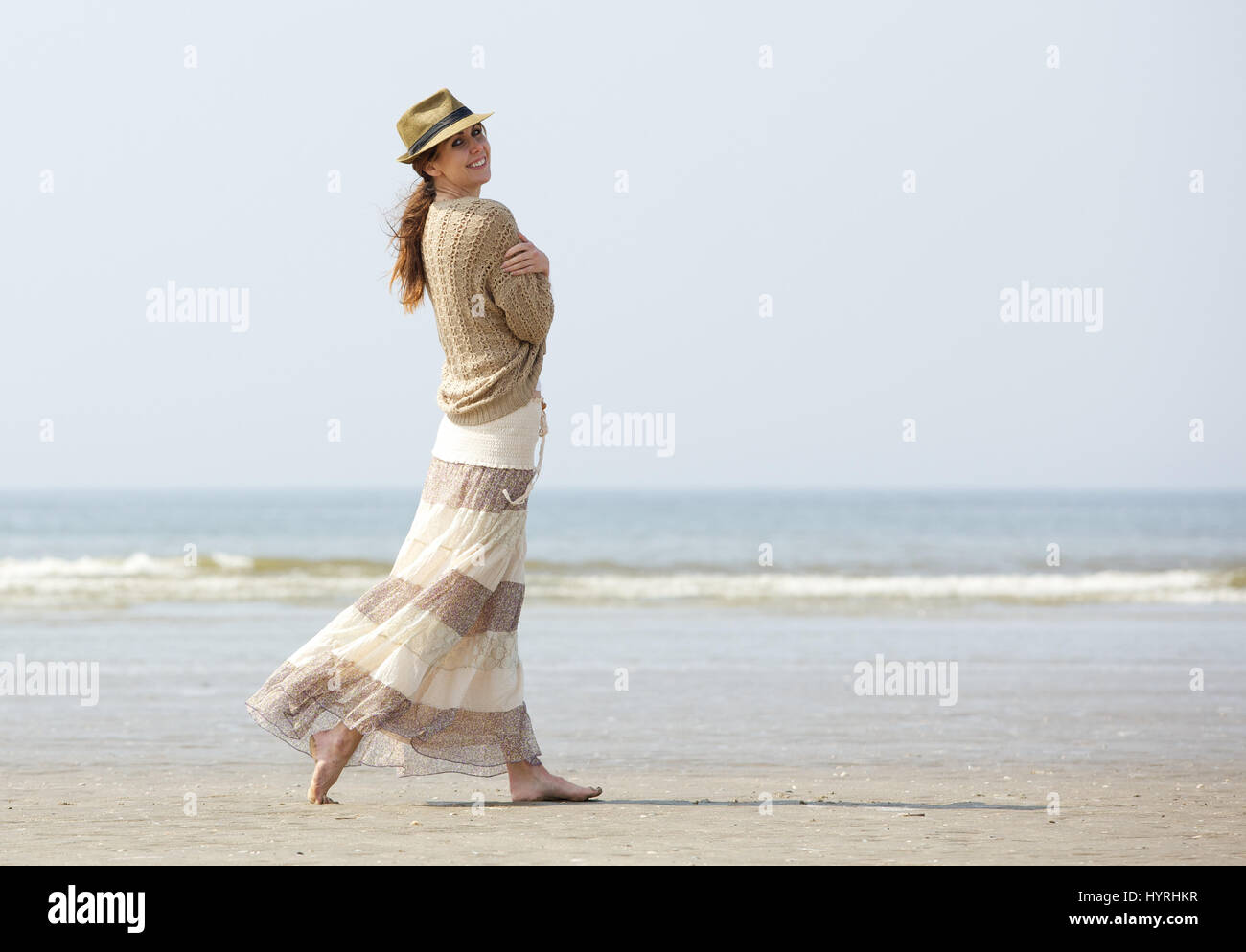Portrait of a smiling woman walking on the beach avec chapeau et robe Banque D'Images