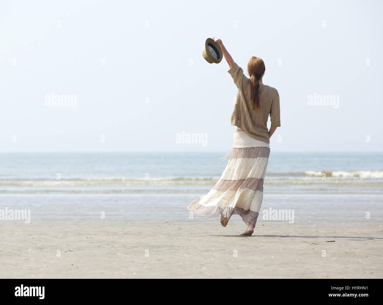 Vue arrière portrait d'une femme marchant sur la plage avec un bras levé Banque D'Images