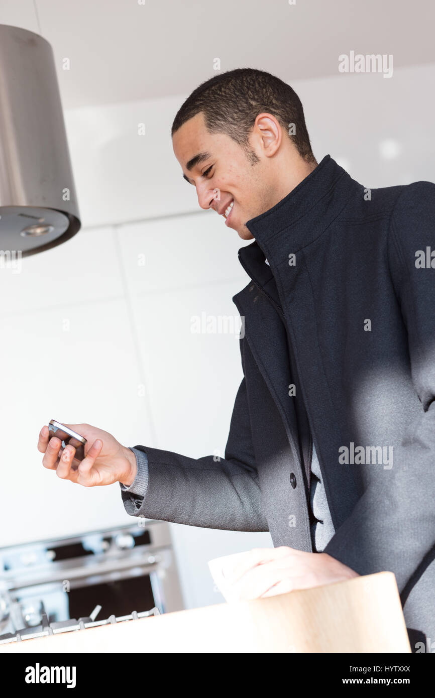 Low angle Vue verticale de l'heureux jeune homme en manteau noir debout dans les portes et de prendre une photographie d'un objet sur la table avec cell phone and smiling Banque D'Images